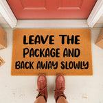 Funny Leave The Package And Back Away Slowly doormat for front porch, featuring bold black text on a natural fiber welcome mat, perfect for delivery drivers and home decor enthusiasts looking for a humorous outdoor entrance rug.