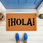 Hola welcome doormat featuring bold black text on a natural fiber coir mat, placed on a white porch in front of a blue door, making a stylish outdoor entrance rug for your home decor, housewarming, or front porch entryway