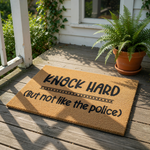 Funny Knock Hard But Not Like The Police doormat made of natural coir fiber, featuring bold black text on a textured brown welcome mat that serves as a humorous front porch decor piece for your home entrance and entryway floor.