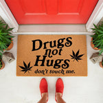 Funny Drugs Not Hugs doormat with cannabis leaf graphics, a natural coir fiber welcome mat for front porch decor that says don't touch me, perfect for a humorous home entrance or a weed themed housewarming gift for a friend.