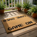 Game Over Game On doormat featuring pixelated black text on a natural coir fiber welcome mat, perfect for a gamer home decor entrance or a fun housewarming front porch rug for video game fans who love retro gaming style floor