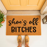 Funny shoe's off bitches doormat for front porch entry, featuring bold black text on a natural coir fiber welcome mat, creating a cheeky housewarming decor piece for your home entrance that keeps floors clean and guests laughing.
