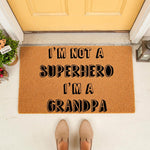 Funny Grandpa doormat featuring bold black text on a natural coir fiber welcome mat, placed on a porch in front of a yellow door, making a humorous home decor entrance rug for a grandfather who is not a superhero but a cool