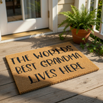 Worlds Best Grandma Lives Here coir doormat, a natural fiber welcome mat for front porch entryways featuring bold black text on a textured brown surface, making a fun home decor piece for a grandmother who loves her house.