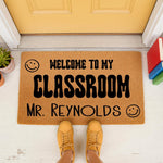 Personalized teacher classroom doormat with a smiley face design, featuring bold black text on a natural coir fiber welcome mat, perfect for a school entrance or teacher appreciation decor on a front porch or classroom door.