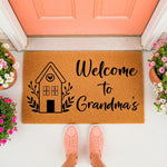 Personalized Grandma welcome doormat featuring a cute house illustration and floral accents, displayed on a porch with pink sneakers and potted flowers, making a stylish coir entry rug for a grandmother home entrance decor.