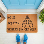 Funny beer doormat with Spanish text No Se Aceptan Visitas Sin Cerveza, featuring a graphic of two clinking beer bottles on a natural coir welcome mat placed on a porch in front of a blue door for a humorous home entrance decor.