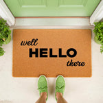 Well Hello There coir doormat for front porch entry, featuring a natural fiber welcome mat with black typography, placed on a white floor in front of a green door with green sneakers standing on the rug for a stylish home