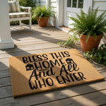 Bless This Home And All Who Enter coir doormat with black text and house icons, a natural fiber welcome mat for front porch decor that adds a warm, inviting touch to your entryway floor and home entrance for guests and family.