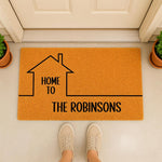 Personalized family name doormat featuring a house outline and custom text on a durable orange fiber mat, perfect for a front porch entrance or housewarming decor that welcomes guests to your home with a stylish and modern design.