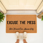 Funny doormat with the text Excuse the Mess We Freed Our House Elf, a natural coir fiber welcome mat for front porch decor that makes a humorous housewarming gift for fantasy fans who love magical home entryways and quirky floor