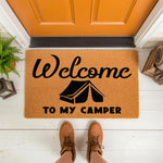 Welcome to My Camper doormat featuring a black tent graphic on natural coir fiber, perfect for outdoor camping decor, RV entryways, or travel trailer porch mats, shown on a white porch floor with brown boots standing in front.