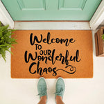 Welcome to Our Wonderful Chaos doormat featuring black script text on a natural fiber mat, placed on a front porch with green shoes visible, making a funny housewarming entry rug for a family home or a unique front door decor
