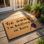 Knitting lover doormat with funny Go away I am knitting in here text, featuring a purple yarn ball and needles graphic on a natural coir welcome mat, perfect for a crafter home entrance or a unique front porch decor floor rug.