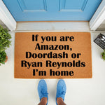 Funny welcome doormat with bold black text on a natural coir fiber mat, featuring a humorous message for delivery drivers and celebrity guests, placed on a porch in front of a blue door for a stylish and welcoming home entrance