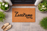 Personalized family name coir doormat for front porch entry, featuring a natural fiber welcome mat with custom text design, placed on a gray tile floor with potted flowers and shoes for a cozy home decor look.