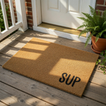 A beige, textured doormat with the word "SUP" printed on it.