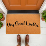 Hey Good Lookin doormat featuring a natural coir fiber texture with bold black script text, placed on a white porch in front of an orange door as a funny welcome mat for your home entryway or front door decor for guests.