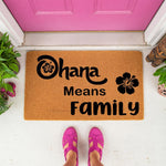 Ohana Means Family doormat featuring a tropical hibiscus flower design on natural coir fiber, perfect as a decorative front porch welcome mat for your home entrance, shown on a white porch with a bright pink door and person in