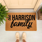 Personalized family name doormat featuring custom text on a natural coir fiber welcome mat, displayed on a front porch entryway with a fern plant and shoes, creating a stylish housewarming decor piece for your home entrance and