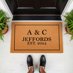 Personalized family name doormat featuring a custom established date, this natural coir fiber welcome mat sits on a front porch and serves as a stylish housewarming decor piece for any home entrance or entryway floor.