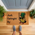 Funny Pineapple Welcome Doormat featuring a cartoon pineapple wearing sunglasses on a swing with the text Just Swingin By, this natural coir fiber outdoor entry rug adds a playful touch to your front porch decor and home entrance.