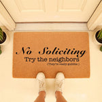 Funny No Soliciting doormat with the text Try the neighbors, They are really gullible, placed on a front porch with white sneakers visible, making this a humorous welcome mat for your home entrance and a great housewarming decor