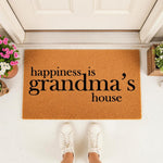 Grandma house doormat with natural coir texture and black text reading happiness is grandma's house, placed on a front porch entryway with white sneakers visible, making a charming outdoor welcome mat for a family home entrance.