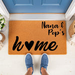 Nana and Pop's home personalized doormat, a natural coir welcome mat for front porch decor featuring black script text and a heart icon, perfect for a housewarming entry rug placed outside a blue front door with blue sneakers