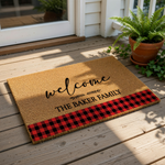 Personalized family name welcome doormat featuring a natural coir fiber texture, black script text, and a festive red and black buffalo plaid border design for a rustic farmhouse porch entrance or home decor entryway floor mat.