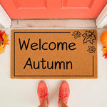 Welcome Autumn coir doormat for fall porch decor, featuring a natural fiber welcome mat with black leaf illustrations, placed at a front door entrance with seasonal orange leaves and a pumpkin for a festive autumn home look.
