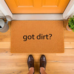 Got Dirt? funny doormat for front porch entry, featuring a natural coir fiber welcome mat with black text, placed on a wood floor in front of an orange door with a metal watering can and a small green plant nearby for home decor.