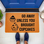 Funny cupcake doormat with the text Go Away Unless You Brought Cupcakes, a natural coir fiber welcome mat for front porch decor that features a humorous food theme for home entryways and makes a quirky housewarming gift for