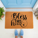 Bless This Home doormat featuring black script text on a natural coir fiber welcome mat, placed on a porch in front of a blue door, making a stylish housewarming entry rug for your front porch decor and home entrance.