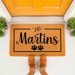 Personalized family name doormat with paw prints, a custom coir welcome mat for pet lovers featuring a black border design, placed on a porch in front of a bright yellow door for a stylish home entrance and entryway decor.