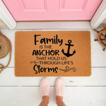 Nautical family anchor doormat with a quote about life's storms, featuring a natural coir welcome mat on a porch with a ship wheel and rope, perfect for a coastal home entrance or a housewarming gift for a family who loves the