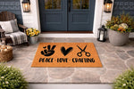 Peace Love Crafting doormat featuring a black graphic of a peace sign, heart, and scissors on a natural coir welcome mat, displayed on a stone porch as a fun hobby-themed front door rug for crafters and makers who love DIY