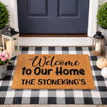 Personalized Welcome to Our Home doormat with custom family name, featuring a natural coir fiber texture on a black and white buffalo plaid rug, perfect for a farmhouse porch entryway decor and outdoor front door entrance mat
