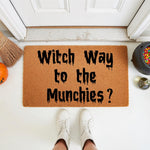 Witch Way to the Munchies Halloween doormat featuring a funny quote in black dripping font on a natural coir fiber mat, perfect for a spooky front porch decor setup with a broom, pumpkin, and candy cauldron for the fall season.