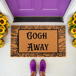 Funny doormat with a swirl art design and the text Gogh Away, this natural coir welcome mat features a humorous pun for your front porch decor, shown on a white floor with purple shoes and bright yellow sunflowers in pots nearby.