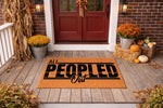 All Peopled Out funny doormat for front porch, featuring a natural coir fiber welcome mat with bold black text, displayed on a rustic wood porch with fall decor, pumpkins, and autumn leaves for a seasonal home entrance entryway.