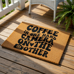 Coffee in one hand camera on the other doormat, a natural coir fiber welcome mat featuring bold black typography and a camera icon, perfect for a photographer home entrance or a stylish front porch decor floor rug.