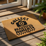 Photography lover doormat with a camera icon and the text Collect Beautiful Moments, featuring a natural coir fiber texture and a black checkered border design for a stylish front porch entry or home decor welcome mat.