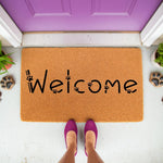 Paw print welcome doormat for pet lovers, featuring a natural coir fiber texture with black text and animal paw accents, placed on a porch in front of a purple door with a person standing on the mat in purple shoes for a home