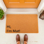 Funny welcome doormat with the text Hi I am Mat printed on a natural coir fiber rug, placed on a front porch entryway as a humorous housewarming decor piece for a home entrance, featuring a durable outdoor floor mat for guests.