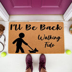 Dog lover doormat with I'll Be Back Walking Fido text and a person walking a dog icon, featuring a natural coir fiber welcome mat for front porch decor that makes a funny housewarming gift for pet owners and dog parents.