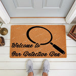 Detective themed welcome doormat featuring a magnifying glass graphic and text reading Welcome to Our Detective Den, this natural coir fiber outdoor welcome mat is a fun entryway rug for mystery lovers and home decor enthusiasts.