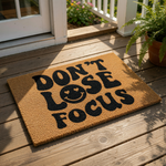 Don't Lose Focus coir doormat with a retro smiley face design, featuring bold black typography on a natural fiber welcome mat that adds a stylish, motivational touch to your front porch entryway decor and home entrance floor.