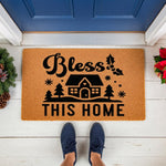Bless This Home Christmas doormat featuring a house, pine trees, and holly design on natural coir fiber, perfect for a holiday front porch entry rug or seasonal welcome mat decor for your front door entrance during the winter