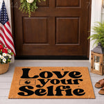 Love Your Selfie doormat featuring bold black typography and a camera icon on a natural coir fiber welcome mat, placed on a front porch entryway to create a fun and stylish home decor look for photography lovers and selfie fans.